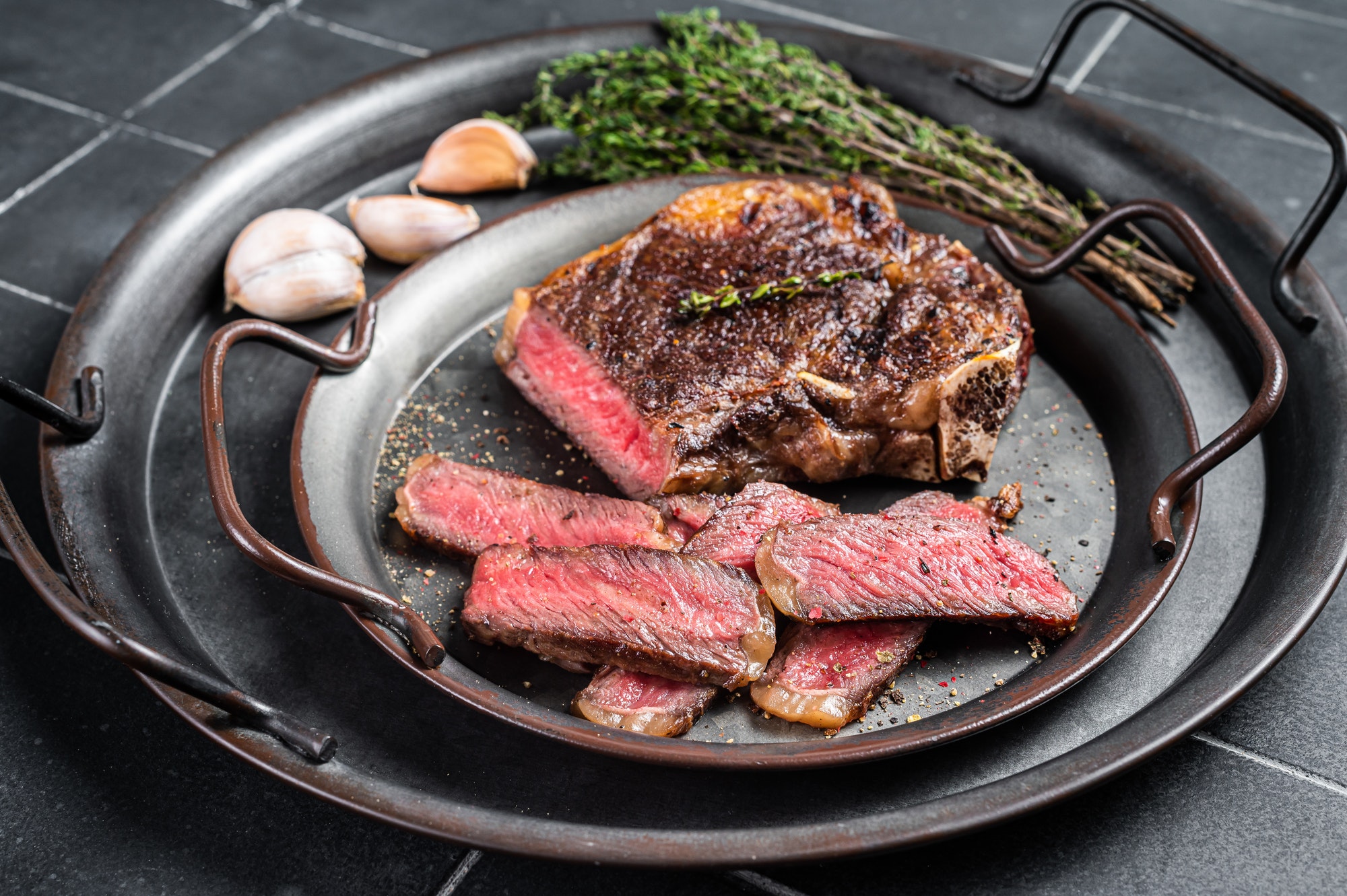 Roasted Sliced Wagyu New York beef meat steak or Striploin steak in a steel tray with herbs.
